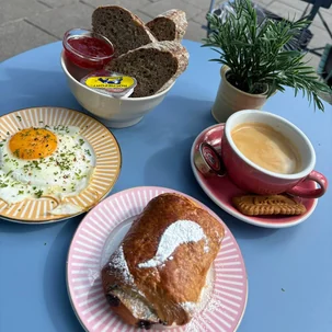 Ontbijtbord met gebakken ei, vers brood, een croissant en een rood kopje koffie bij Pepper