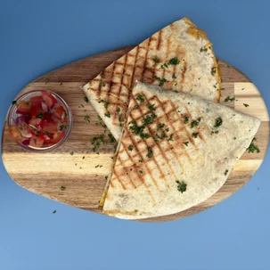 Twee driehoekige quesadilla's met gesmolten kaas en verse tomatensalsa op een houten plank